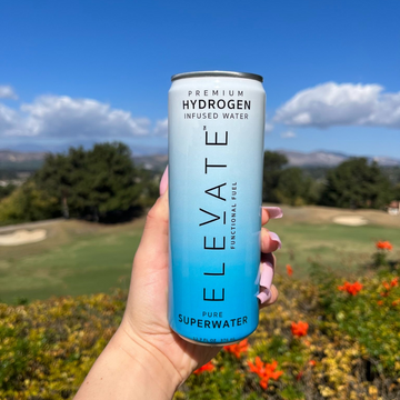 woman holding ELEVATE hydrogen-infused SuperWater on a sunny day surrounded by flowers on a golf course