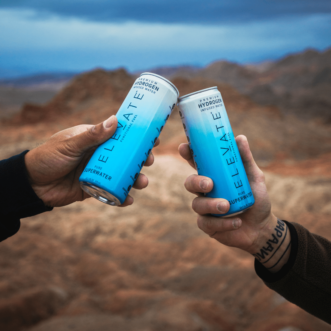 Two people holding ELEVATE Hydrogen-Infused SuperWater Cans, about to drink together, in an Arizona valley.